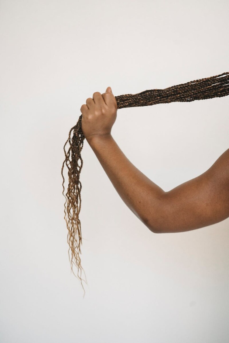 crop faceless ethnic person touching ponytail of african braids