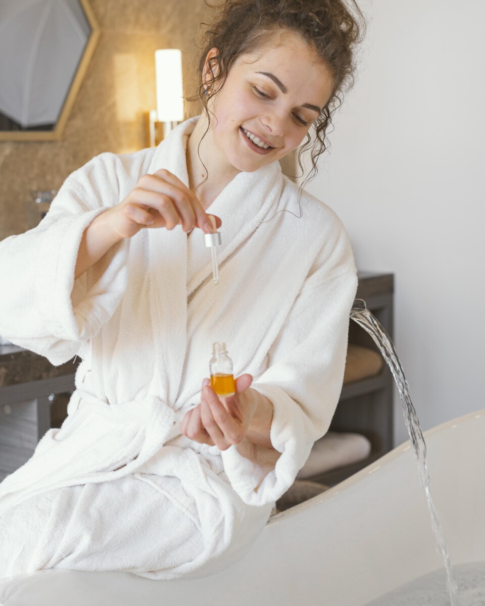 woman bathrobe pouring serum bathtub 10 Essential Oils Every Bride Needs for Pre-Wedding Relaxation