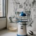 Composition of white and blue miniature lighthouse tower with creative pencil painting placed on table with scattered seashells near window