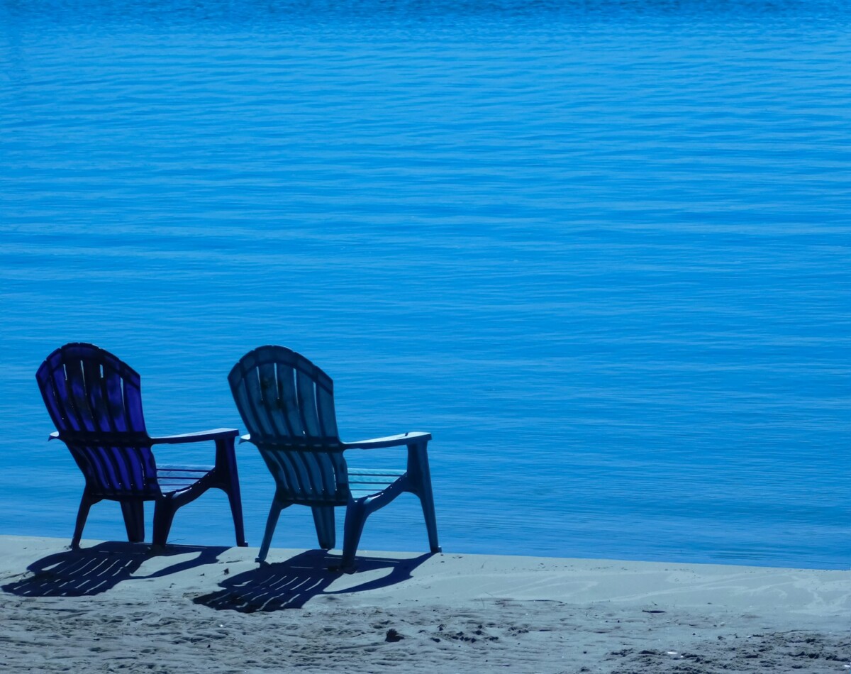 a couple of chairs sitting on top of a sandy beach