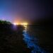 a night time view of a beach with lights in the water
