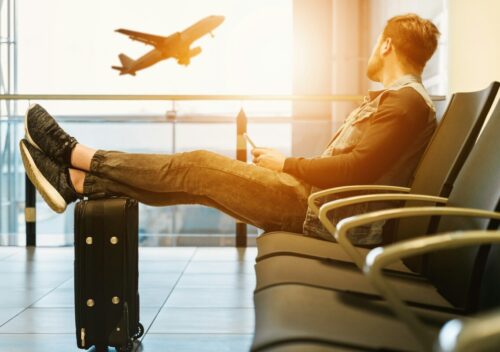man sitting on gang chair with feet on luggage looking at airplane